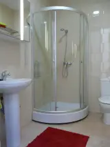 Bathroom with corner glass shower cubicle, toilet, pedestal basin and red bath mat